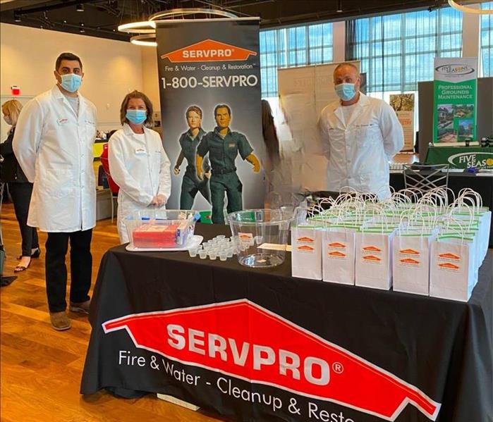 servpro employees in white lab coats standing behind table with black table cloth with servpro logo